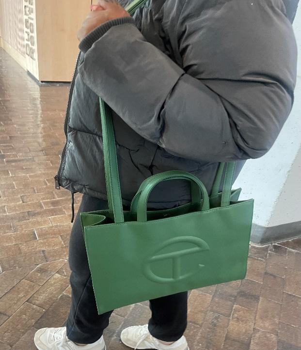 A person in a coat holding a green purse

Description automatically generated