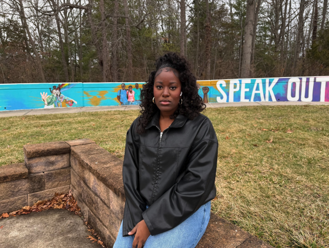 Shaquana Ricketts, a junior at SUNY Old Westbury, sits in front of a colorful campus mural reading “speak out” reflecting a message of student voice and expression. PHOTO BY: JULIA-LYN CHEATHAM