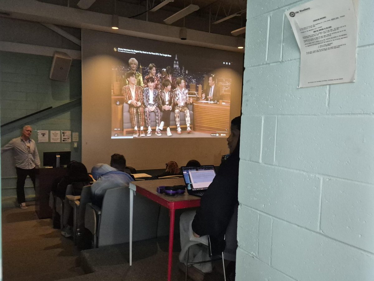 SUNY Old Westbury Professor Paul Carlon on March 13, 2026, showing a video from his lecture on K-pop in the campus center at SUNY Old Westbury. PHOTO BY: MICHELLE MORENO