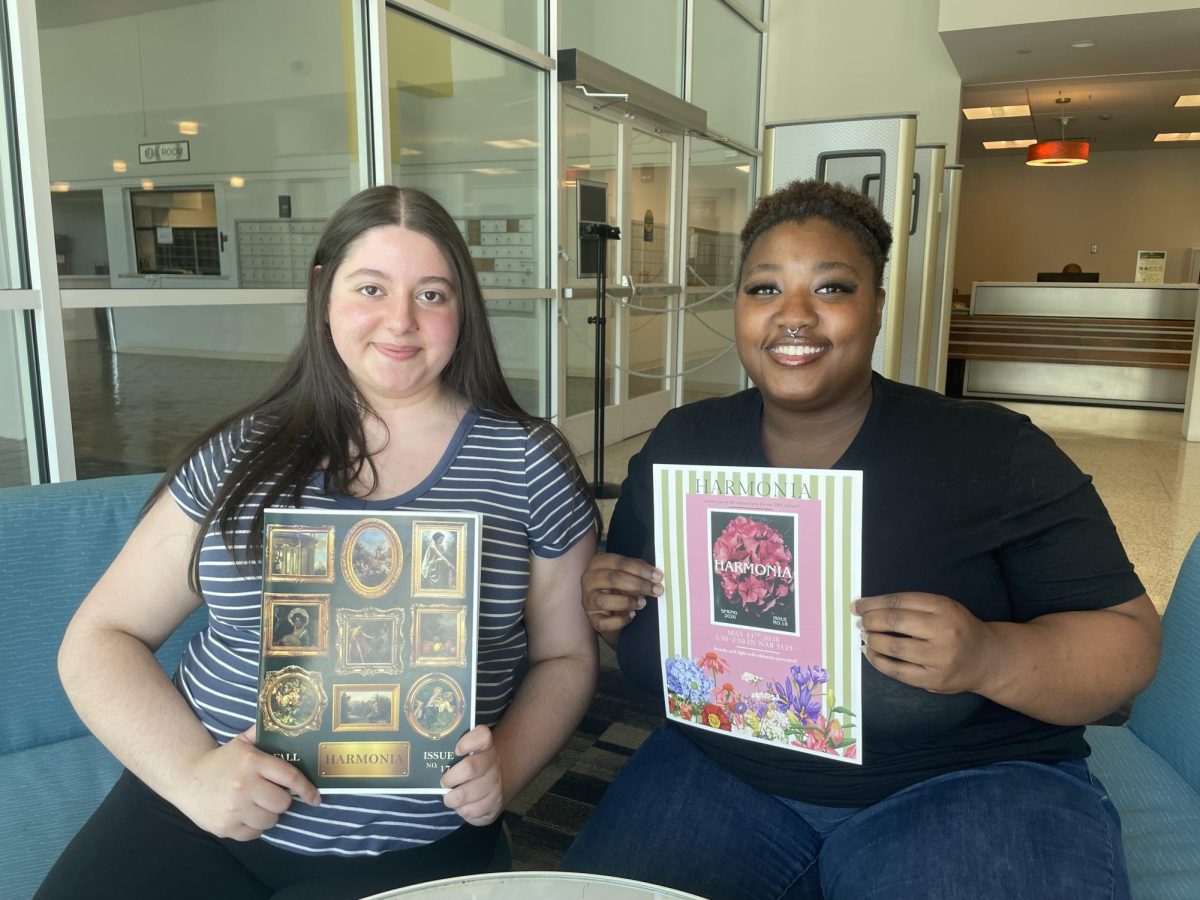 Lori Yamond (left) and Brianna Leconte (right) sit in the SUNY Old Westbury library. Yamond holds up a previous edition of the Harmonia/Discordia publication. Leconte holds up a poster of the Harmonia/Discordia 2026 release party poster, on April 27, 2026. PHOTO BY: ANN BUNCH